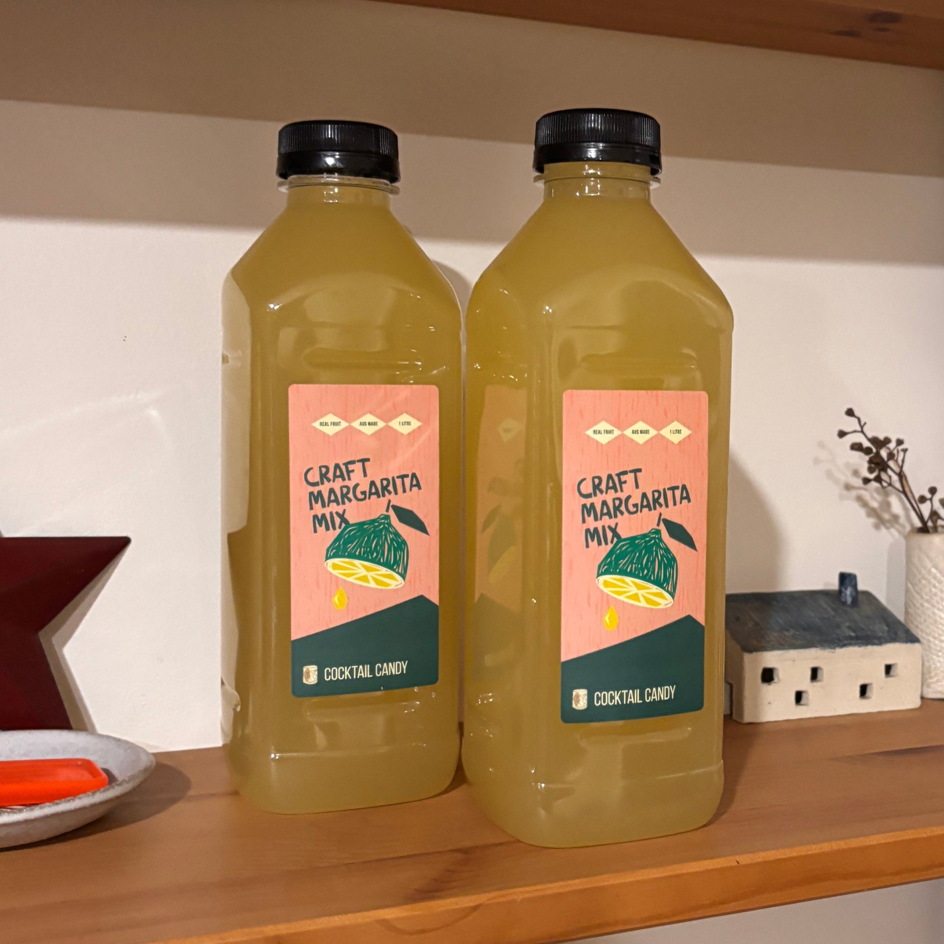 Two bottles of juice on a wooden shelf with various items around