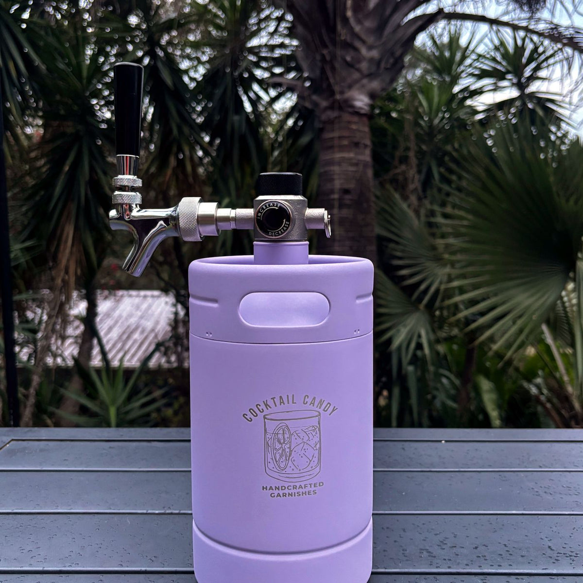 Violet Hour Purple Cocktail Candy Mini Keg with its tap and regulator on an outdoor table, palms behind